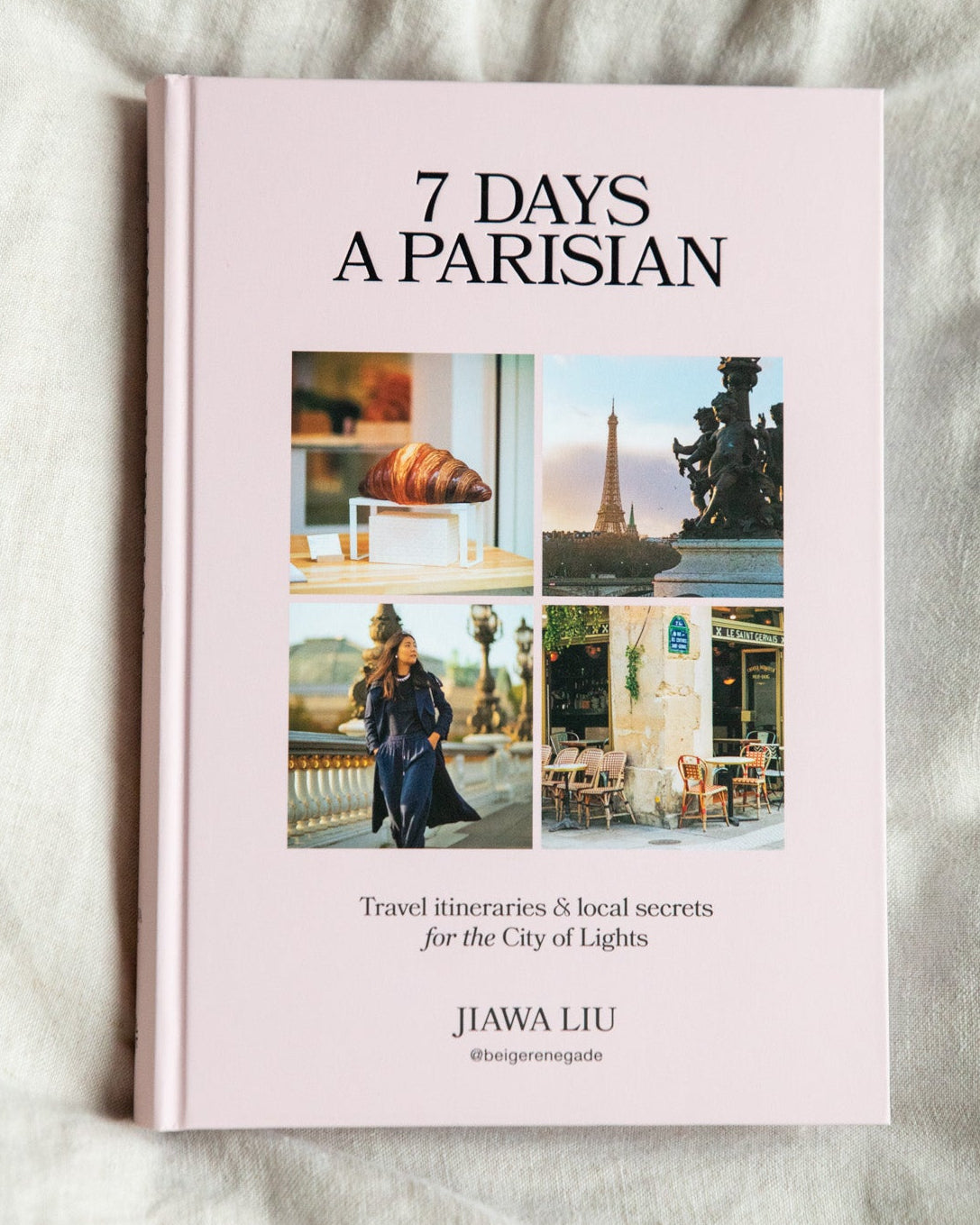 A pink hardcover book titled '7 DAYS A PARISIAN' by Jiawa Liu, featuring a collage of Paris-themed travel photos on the cover, photographed flat on a textured white fabric background.